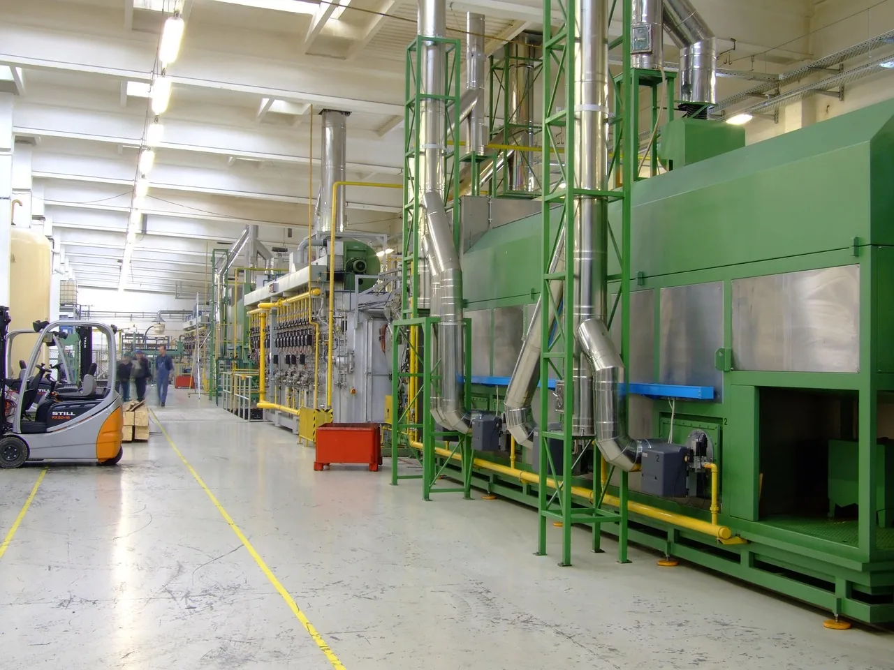 Grande halle industrielle avec ligne de production verte et chariot élévateur