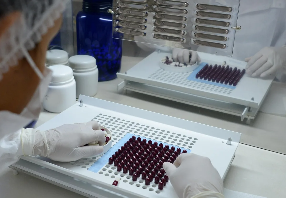 Opératrice gantée remplissant un plateau de flacons en production pharmaceutique