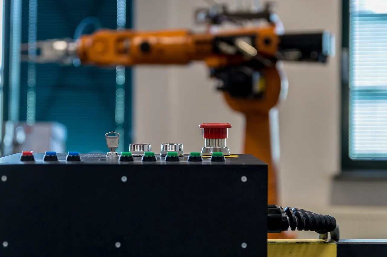 Bras de robot industriel orange derrière un pupitre de commande avec arrêt d'urgence